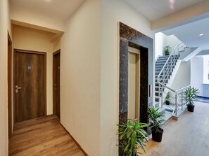 A modern hotel hallway with wooden flooring, a marble accent wall, and a staircase leading to an upper level.