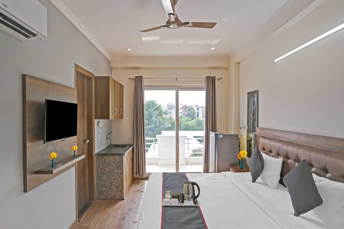 A hotel room with a bed, a TV, a kitchenette, and a balcony with a view of buildings.