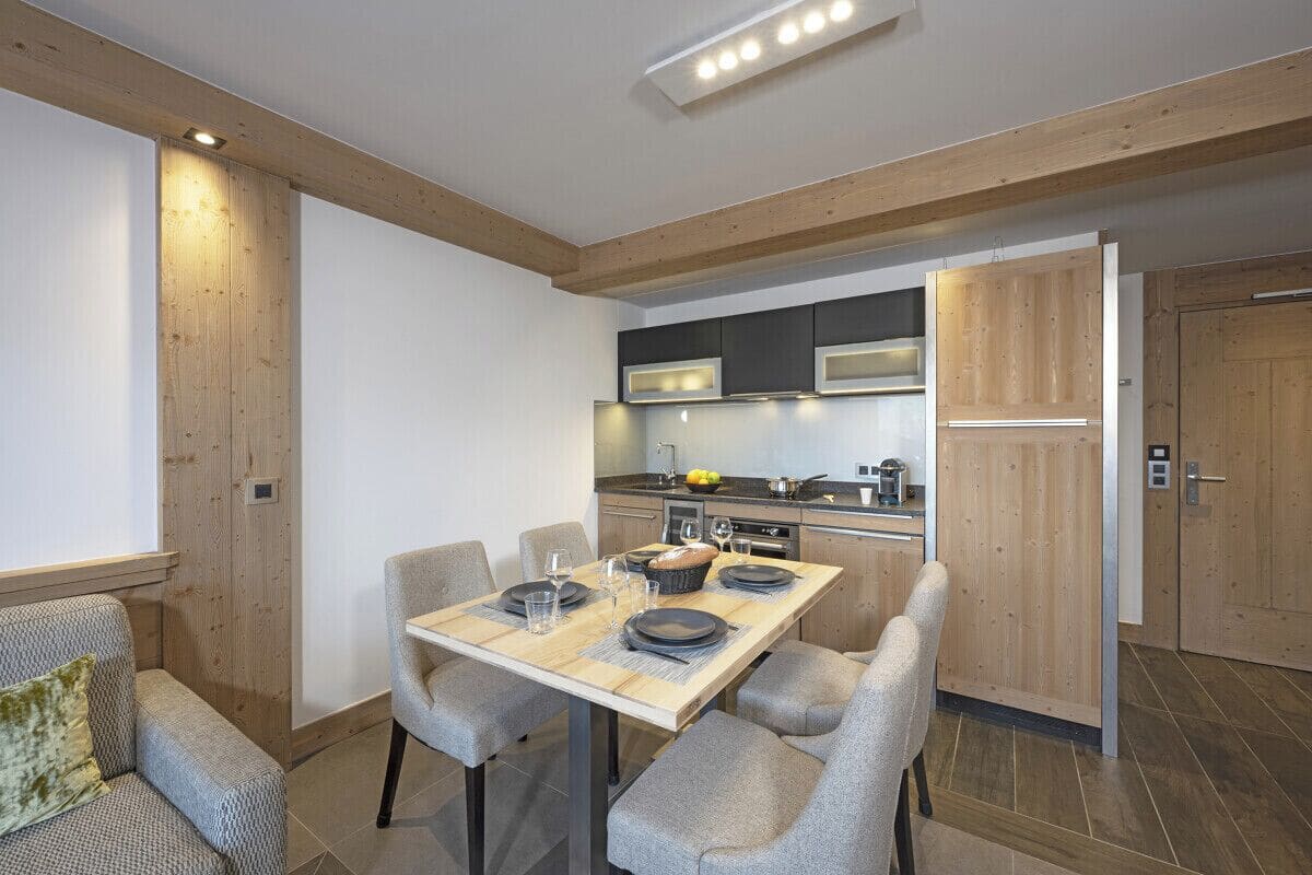 A modern kitchen with wooden cabinets, a dining table set for four, and a built-in oven.