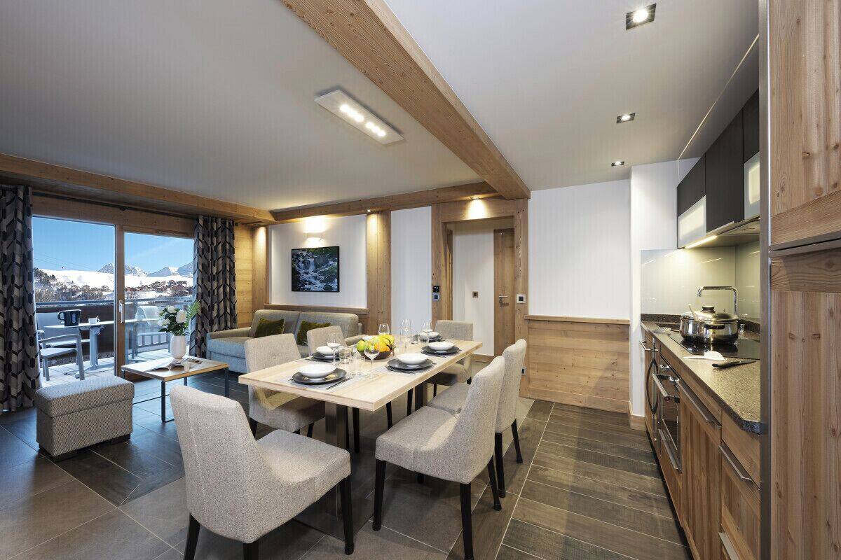 A modern kitchen with wooden cabinets, a dining area with a table set for four, and a large window offering a view of the mountains.