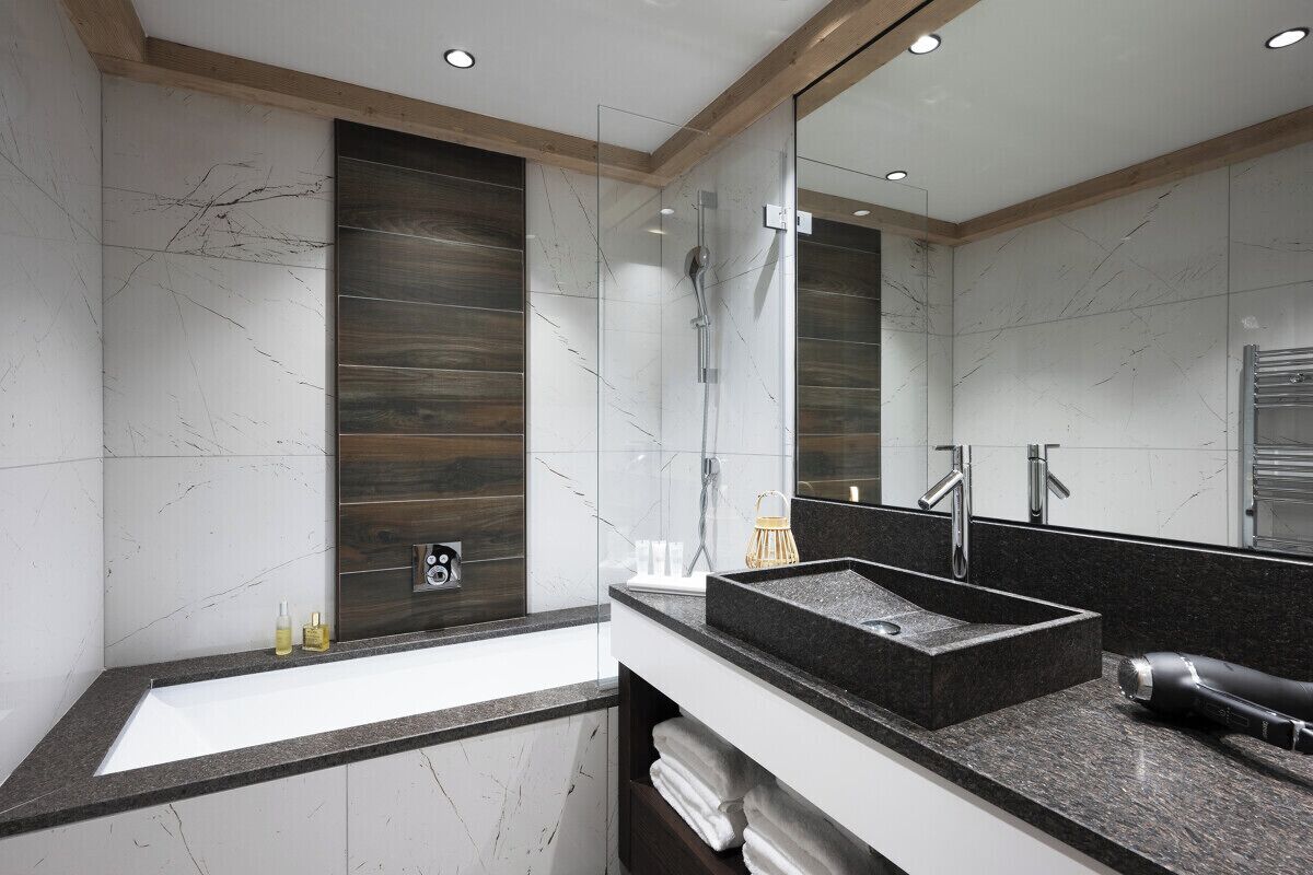 Un baño moderno con un espejo grande, un lavabo negro y una ducha.