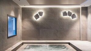 A modern spa room with a large bathtub, recessed wall lighting, and a window with a blue view. - MGM Hôtels & Résidences – Résidence Manaka (La Plagne-Tarentaise)