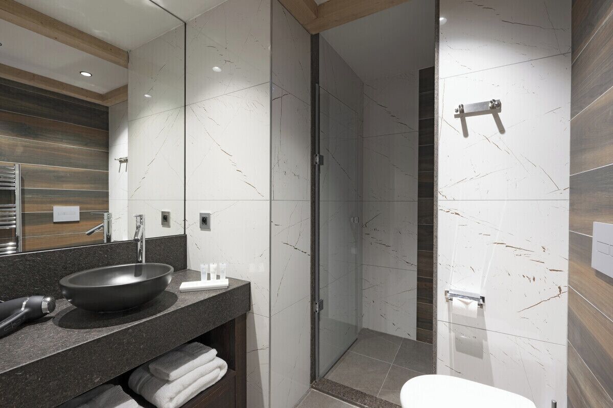 A modern bathroom with a large mirror, a black basin, and a shower area.