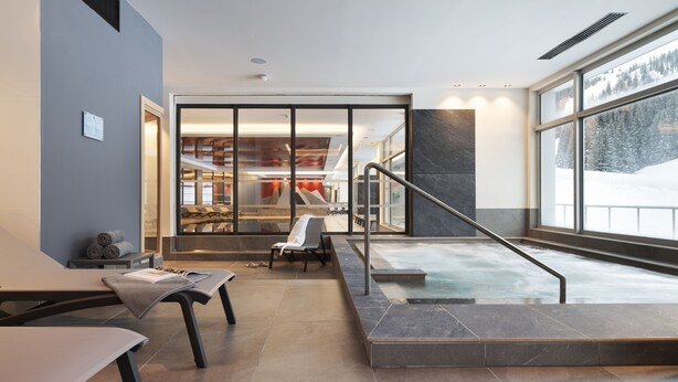 Zona de spa con jacuzzi, asientos y vistas a un paisaje nevado.