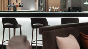 Zona de bar moderna con mostrador, taburetes y una variedad de botellas.