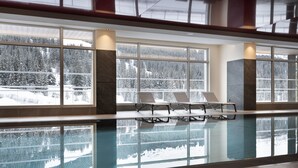 Una piscina interior con paredes de vidrio transparente que reflejan vistas de un bosque nevado.