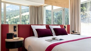 Habitación de hotel con una cama grande, cabecera roja y vistas a una cadena montañosa boscosa.