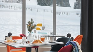 Comedor con una mesa dispuesta para dos, sillas y vistas a un paisaje montañoso nevado a través de amplias ventanas.