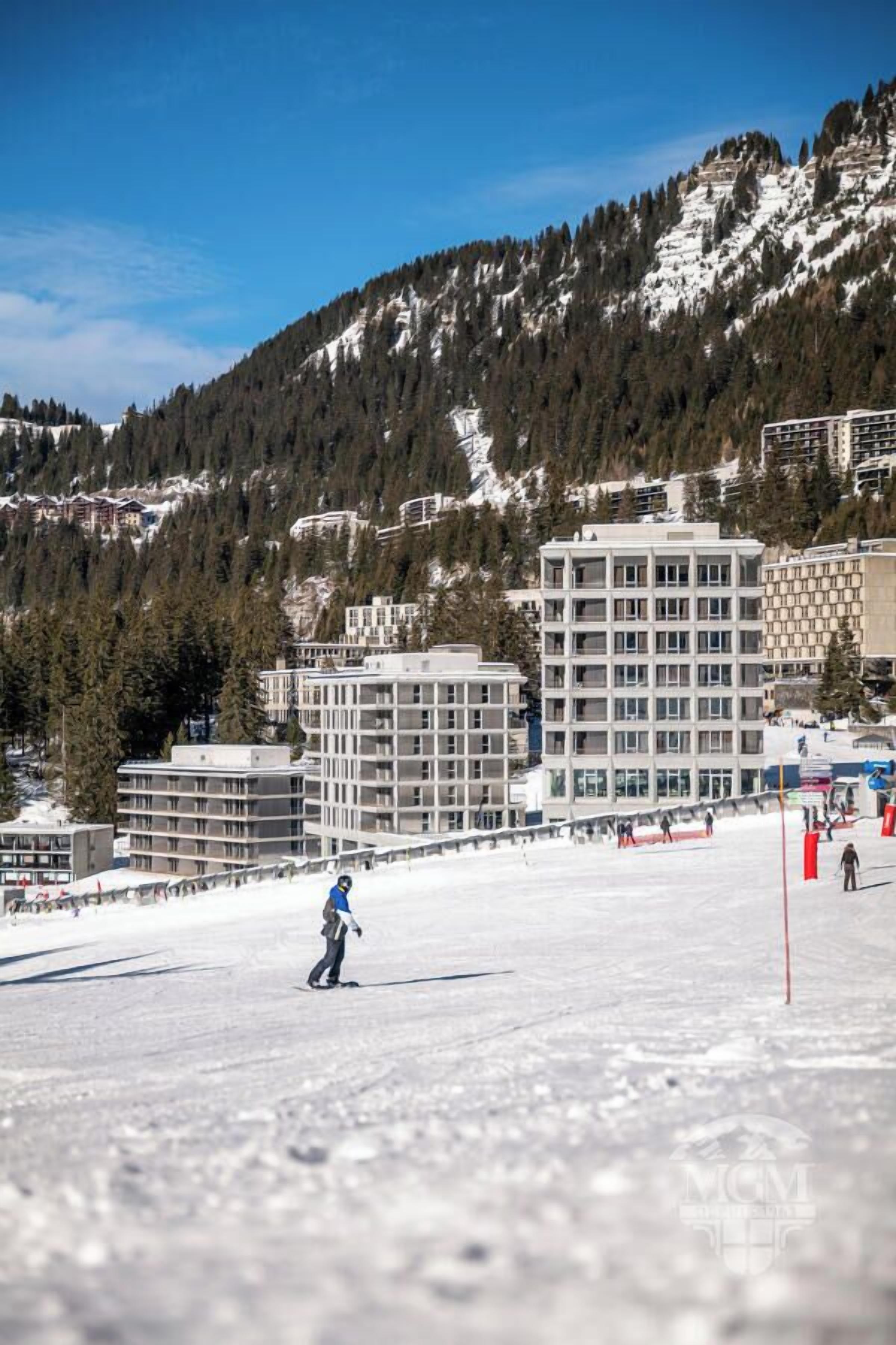 A ski resort with buildings, a snowy slope, and a mountain backdrop.