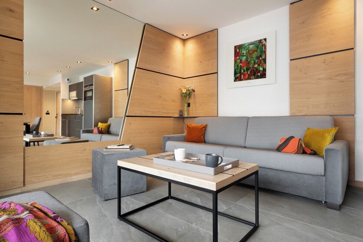 A modern living room with a grey sofa, a coffee table, and a kitchen in the background.