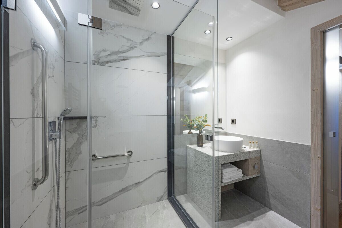 Un baño moderno con ducha envuelta en vidrio, lavamanos con encimera de granito y suelo de mármol.