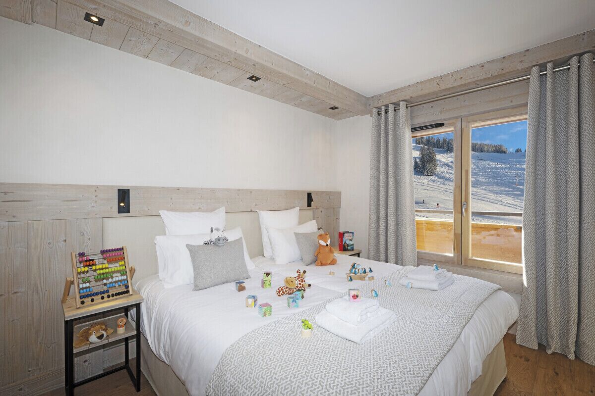 Een slaapkamer met een bed, kussens, een nachtkastje, een houten hoofdbord, een raam met gordijnen en uitzicht op een besneeerd landschap.