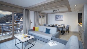 Een moderne woonkamer met een grijze bank, een eettafel en een besneeerd landschap door grote ramen.