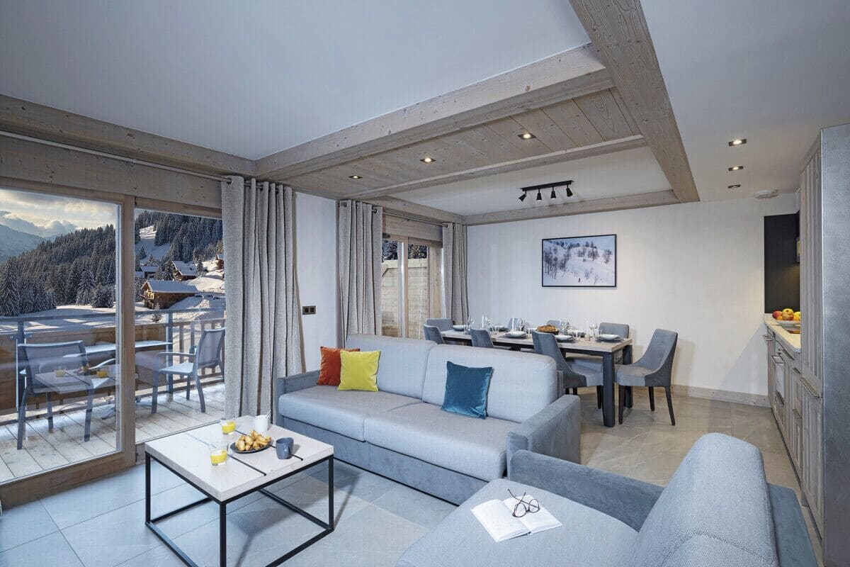 Una sala de estar moderna con un sofá gris, una mesa de comedor y vistas a un paisaje nevado a través de amplios ventanales.