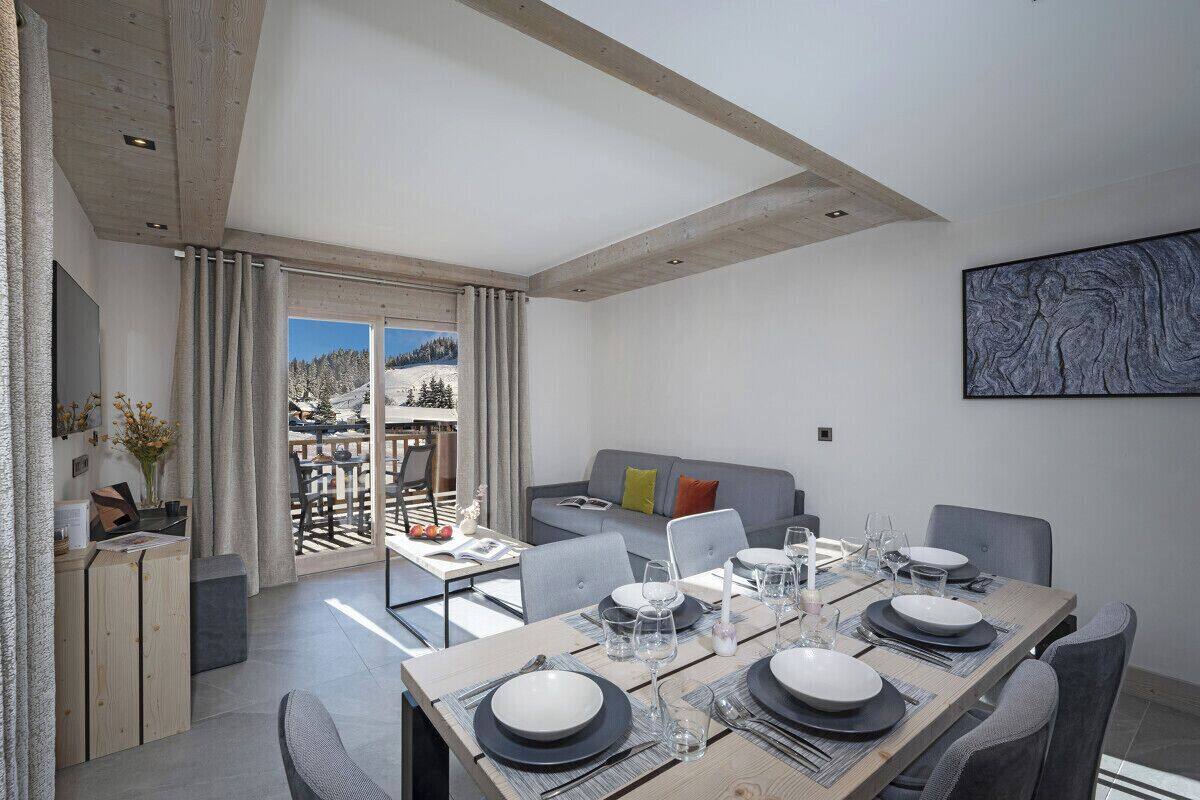 Un moderno comedor con una mesa de madera dispuesta para cuatro, un sofá con cojines y vistas a un paisaje nevado a través de amplios ventanales.