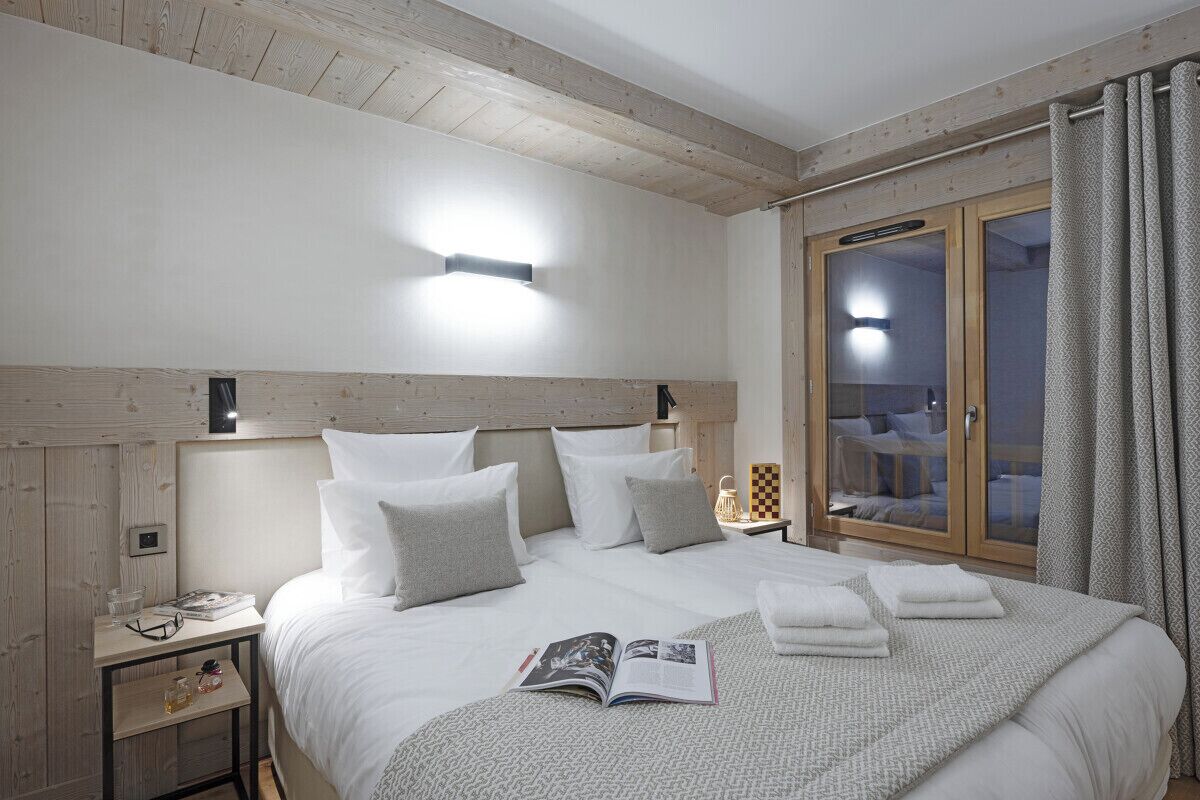Une chambre à coucher avec un grand lit, des tables de chevet, une commode, une fenêtre avec des rideaux et un plafond en bois.