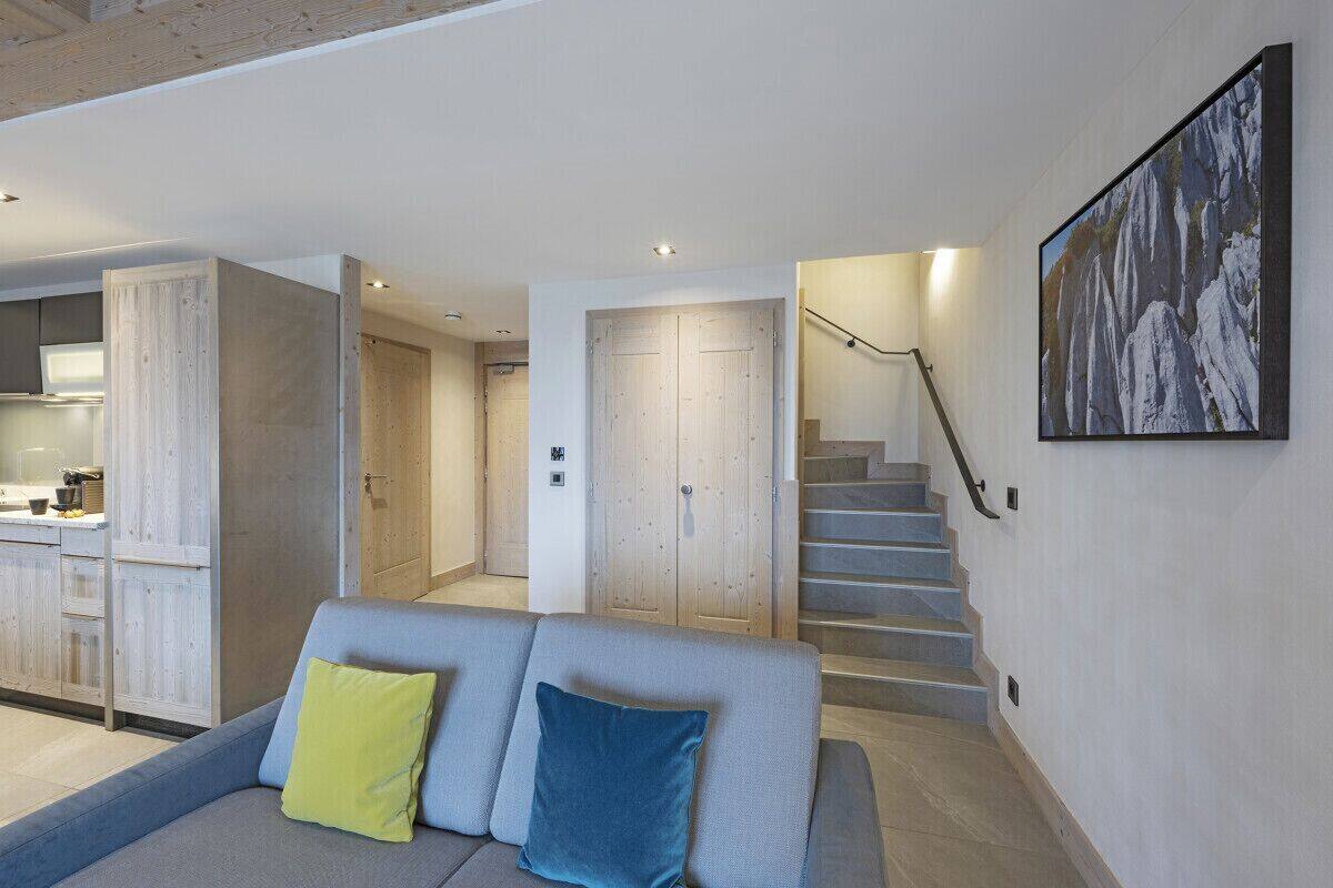 Una sala moderna con un sofá gris, armarios de madera y una escalera que sube a otro nivel.