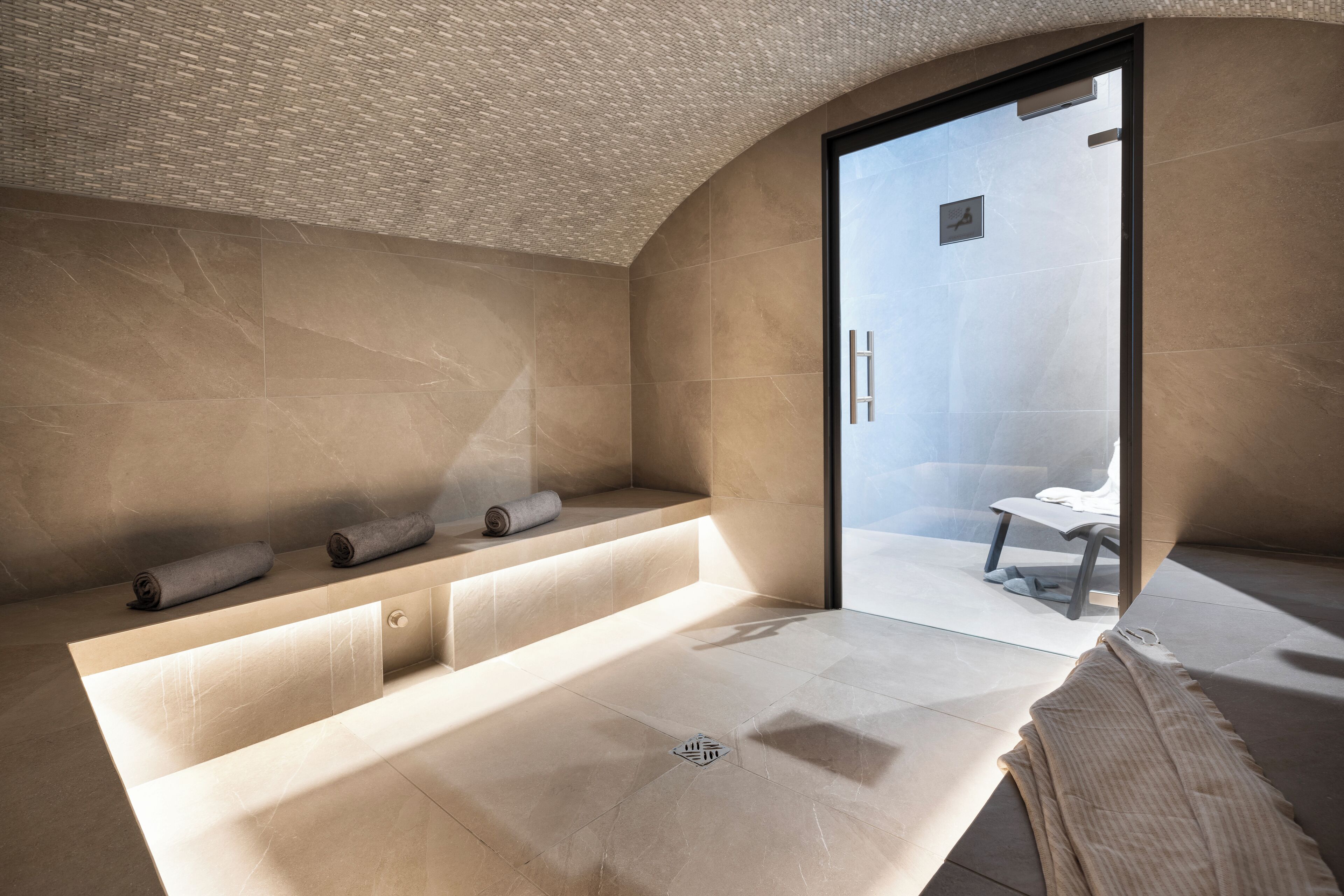 Moderni spa-huone, jossa on kiviseinä, penkki ja pyyhekoukku.
