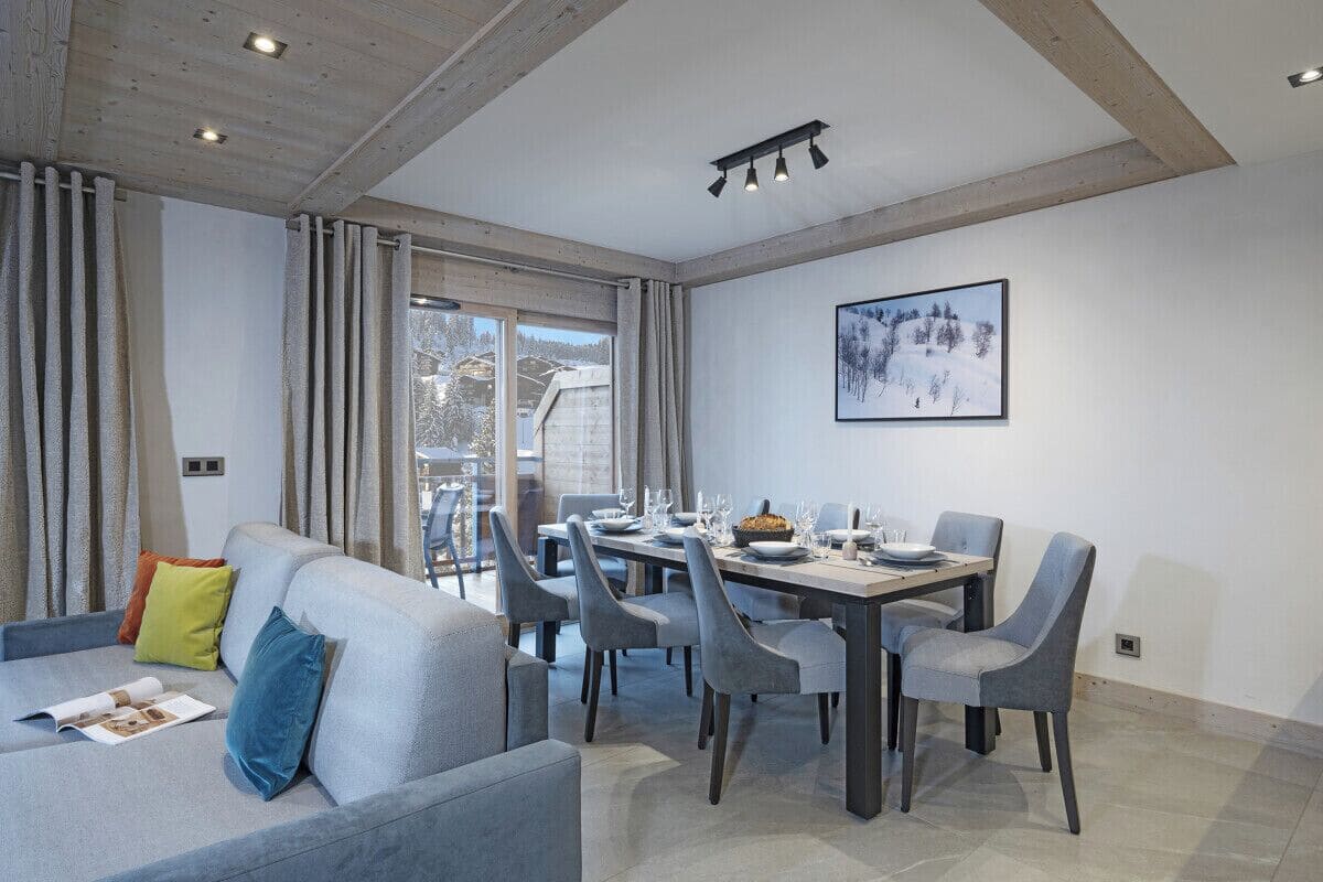 Una sala de estar moderna con un sofá, una mesa de comedor y sillas. Hay un ventanal con cortinas, un cuadro en la pared y un balcón visible a través del ventanal.
