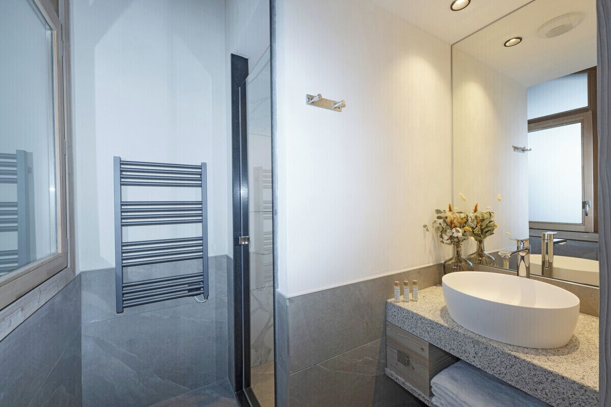 A modern bathroom with a glass shower enclosure, a freestanding towel rack, a large oval sink, and a mirror above the sink.