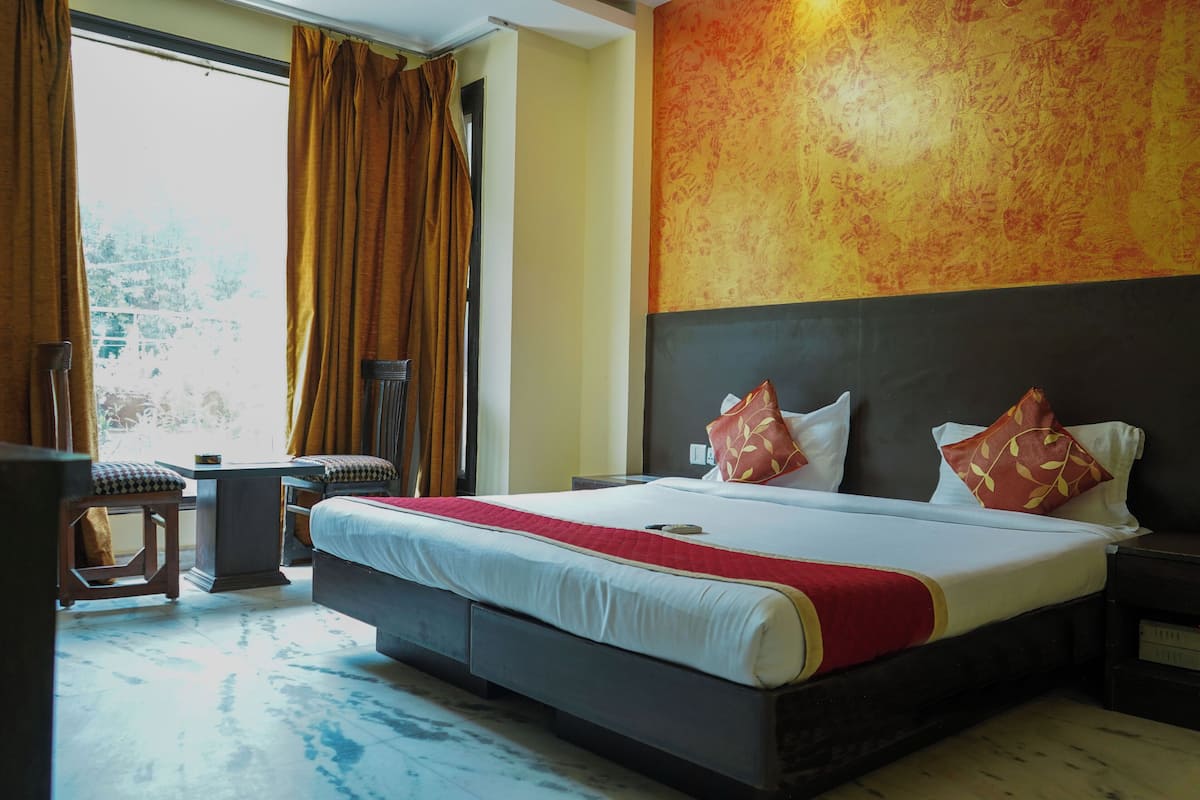 A hotel room with a large bed, a nightstand, a chair, and a view of the outdoors.