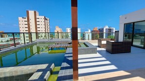 Une piscine sur le toit offrant une vue dégagée sur les gratte-ciel de la ville, des meubles de jardin modernes et un espace de restauration entièrement vitré.