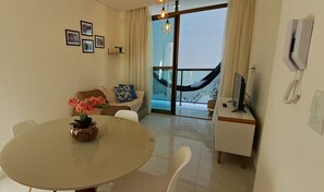 A modern living room with a dining table, a sofa, a hammock, and a TV on a stand. - VIAMAR BEACH HOUSE (Cabedelo)