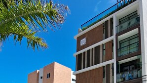 Un hôtel moderne à plusieurs étages, dont la façade est un mélange de briques et de verre, avec un logo bien visible et une entrée sécurisée par un portail.