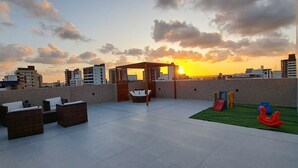 Une terrasse sur le toit, dotée d’un espace salon, d’une aire de jeux et offrant une vue sur le coucher de soleil au-dessus de la ville.