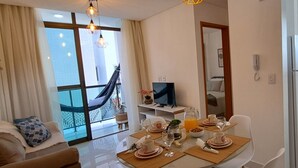 Une chambre d’hôtel moderne dotée d’un coin repas, d’une télévision et d’un balcon avec un hamac.