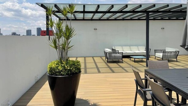 Eine Dachterrasse mit einem Glaspergola, Sitzgelegenheiten im Freien und einem großen Topfpflanzen.