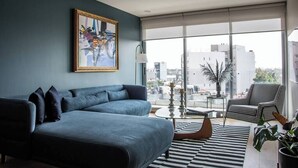 Ein modernes Wohnzimmer mit einem blauen Sofa, einem schwarz-weißen Streifen Teppich und Blick auf die Stadt durch große Fenster.
