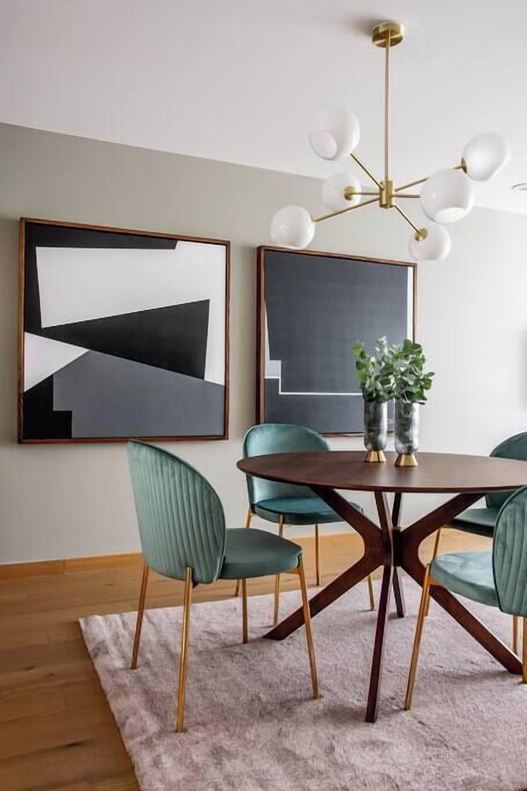A dining area with a round table, green upholstered chairs, and two abstract paintings on the wall.