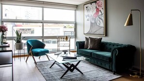 A modern living room with a teal armchair, a green sofa, a glass coffee table, and a large floral painting on the wall. - Great location, pool, rooftop, gym, 24/7 security (Ciudad de México)