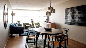 Een moderne eetruimte met een ronde tafel, zwarte stoelen en hanglampen. Achtergrond toont een bank en salontafel.