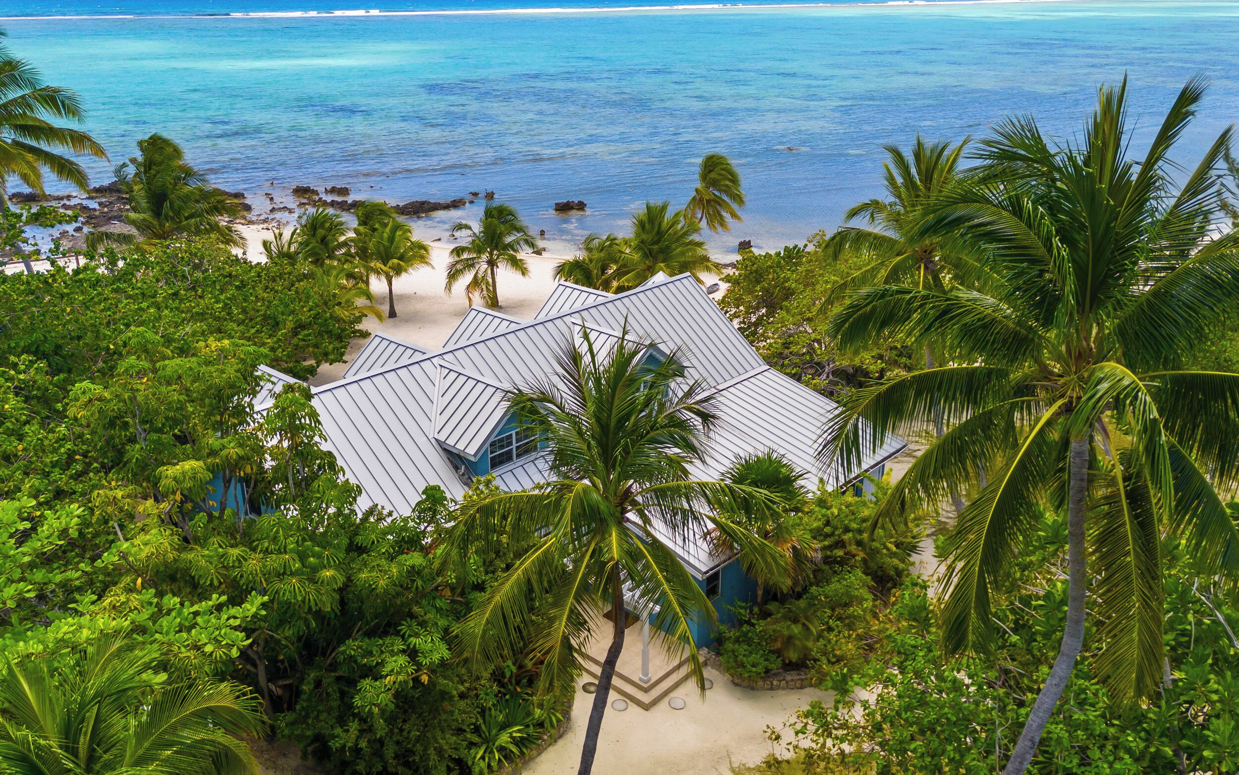 Une propriété située en bord de mer, avec une maison moderne, entourée d’une végétation luxuriante et de palmiers, et offrant une vue sur l’océan.