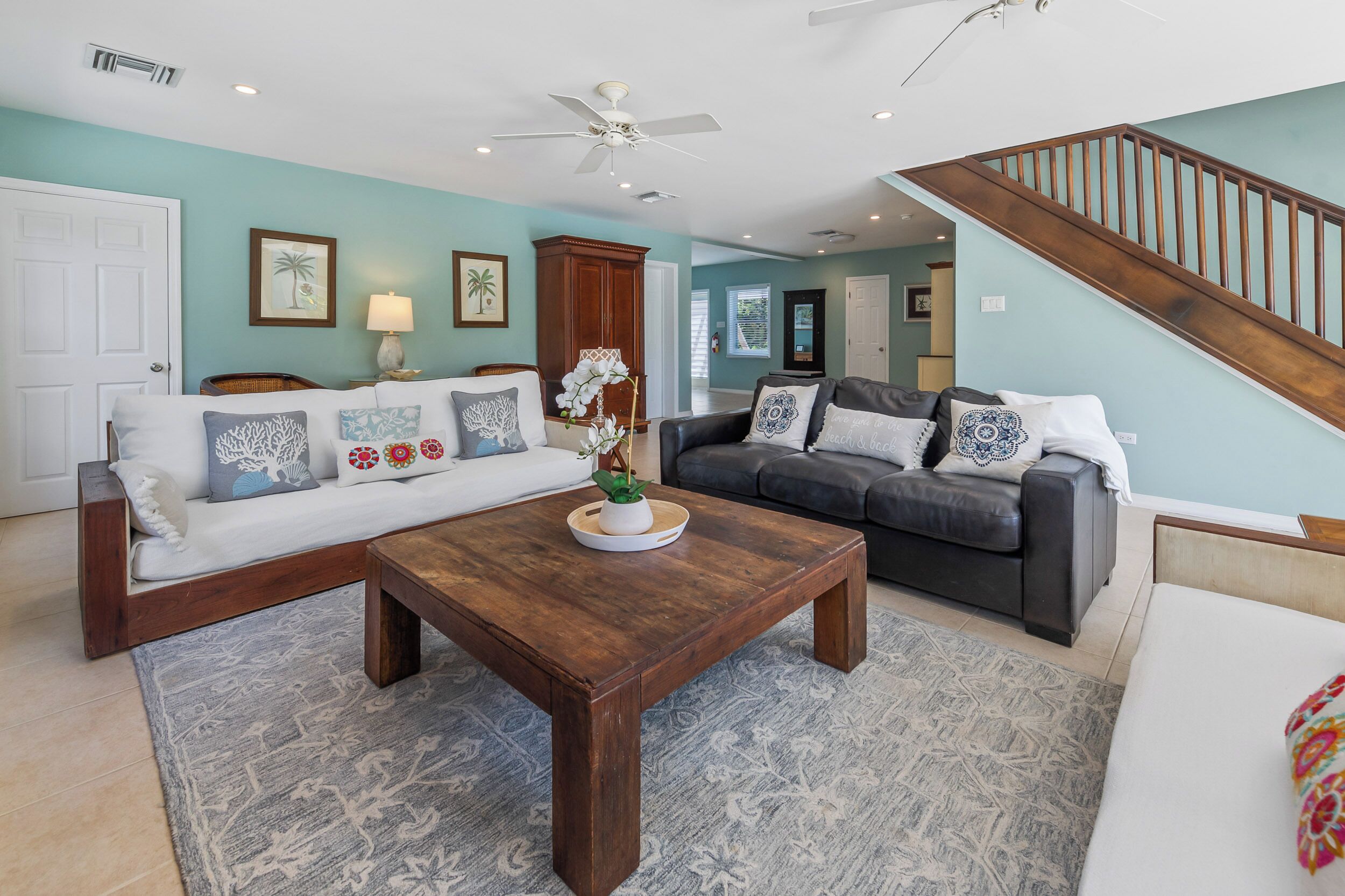 A living room with a white sofa, a dark sofa, a wooden coffee table, and a staircase.
