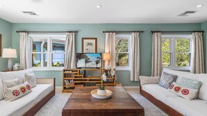 A living room with two sofas, a coffee table, a TV, and a bookshelf. - Pease Bay Manor is a private, secluded beachfront villa - call Cayman Villas (Bodden Town)