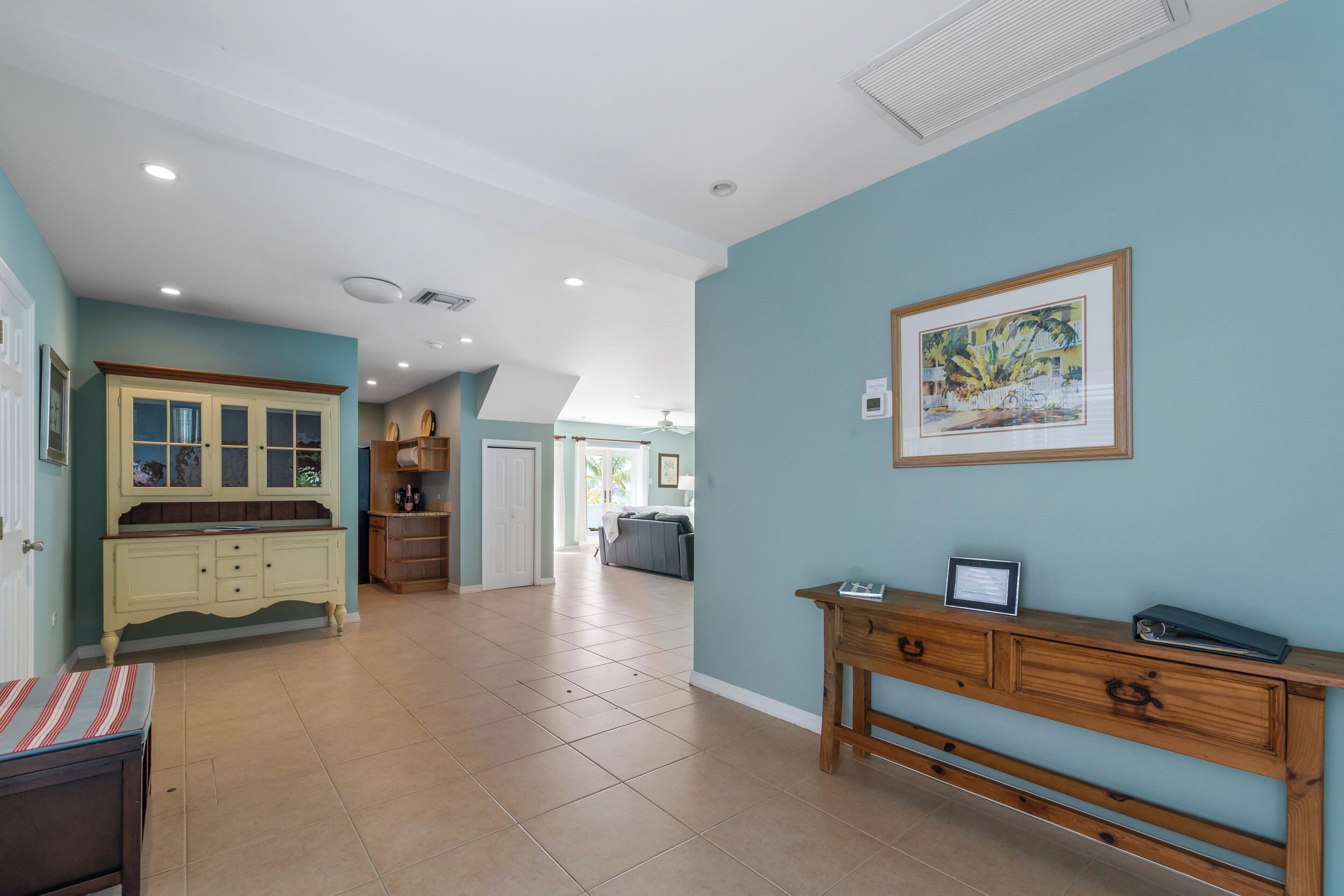 A spacious room with a large wooden cabinet, a framed picture on the wall, and a view into another room.