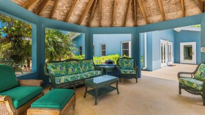 A covered outdoor seating area with wicker furniture and a thatched roof. - Pease Bay Manor is a private, secluded beachfront villa - call Cayman Villas (Bodden Town)