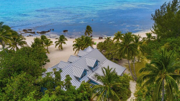 A beach view with a building surrounded by palm trees. - Pease Bay Manor is a private, secluded beachfront villa - call Cayman Villas (Bodden Town)