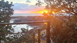 Une terrasse en bois avec une rambarde en corde, donnant sur une zone riveraine et offrant une vue sur le coucher de soleil.