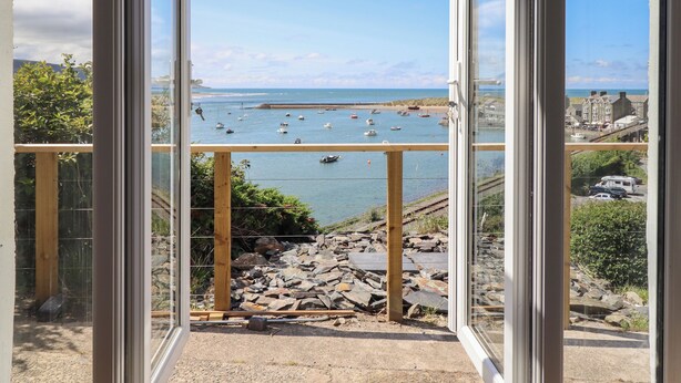 Une vue depuis un balcon donnant sur une zone côtière, avec des bateaux, une côte rocheuse et des bâtiments visibles au loin.