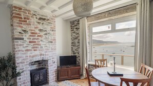Une pièce dotée d’une cheminée en pierre, d’un téléviseur, d’une table à manger avec des chaises, et offrant une vue sur la mer grâce à une grande fenêtre.