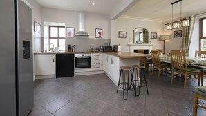 A modern kitchen with white cabinets, a built-in oven, and a dishwasher. There is a dining area with wooden chairs and a table.