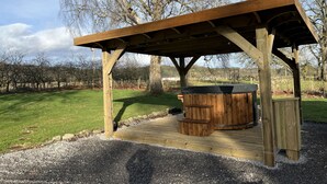 A wooden gazebo with a hot tub, surrounded by a gravel area and a grassy field.