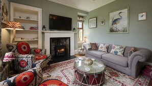 A living room with a fireplace, sofa, patterned rug, and a drum table.