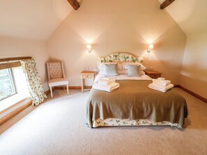 A bedroom with a large bed, two bedside tables, a chair, and a window with curtains.
