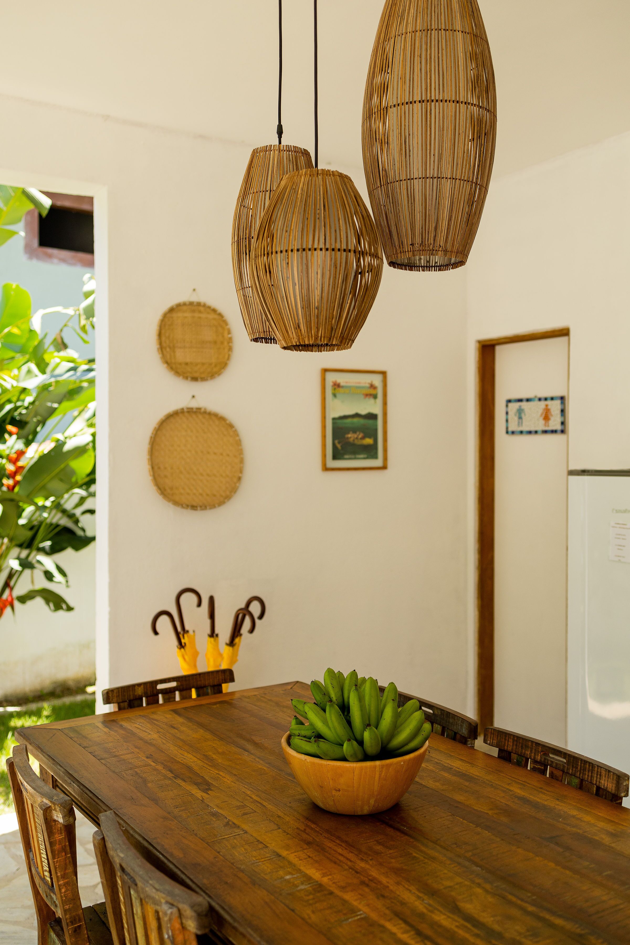 A wooden dining table with a bowl of bananas, wicker pendant lights, and a whiteboard with writing.