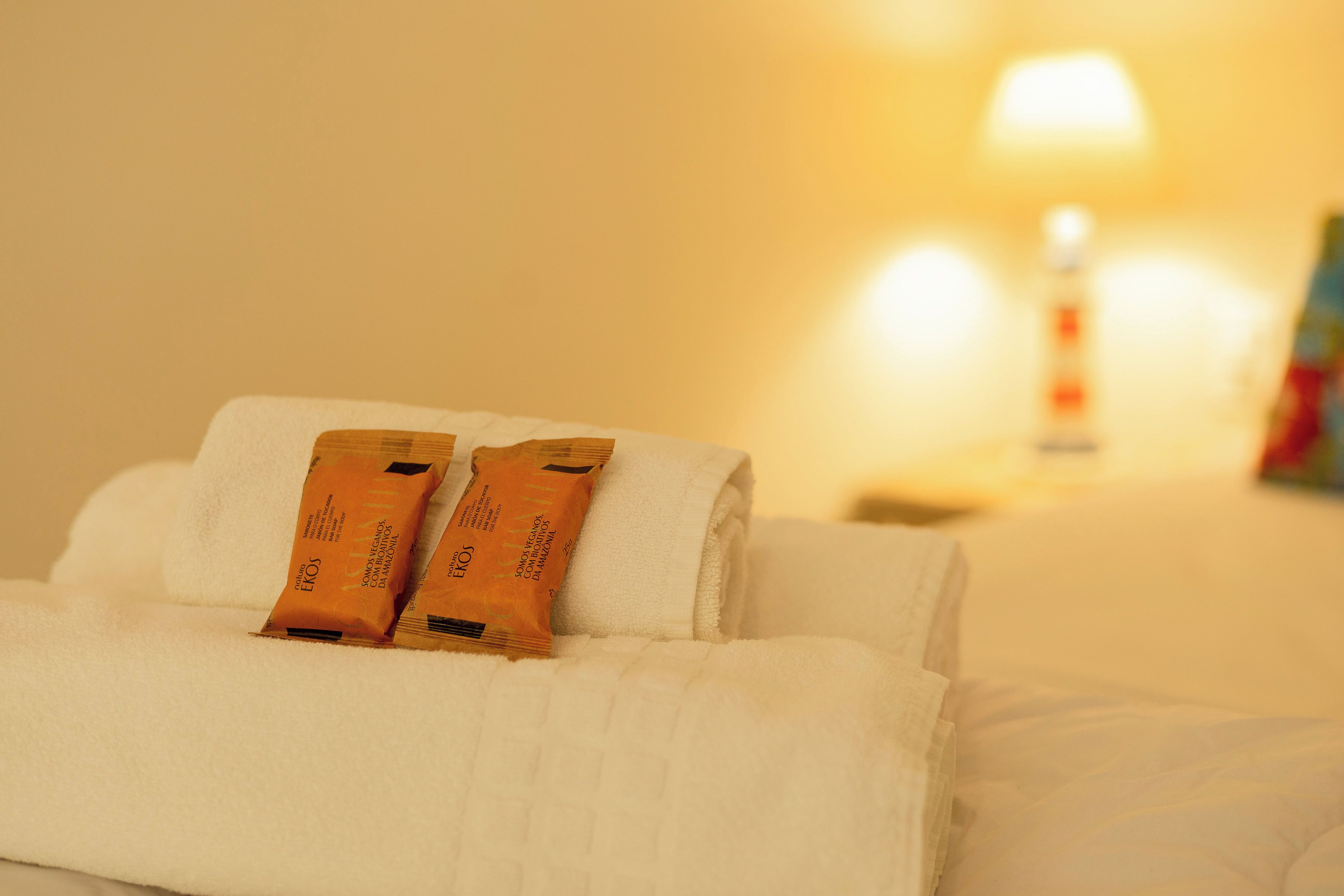 Une serviette blanche, soigneusement pliée, avec deux petits paquets orange posés dessus, sur un lit.